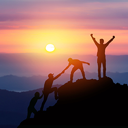 A group of people climbing a mountain at sunset, helping each other to get to the top. 