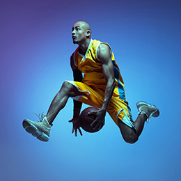 Professional basketballer, in the air, passing the ball under his body.