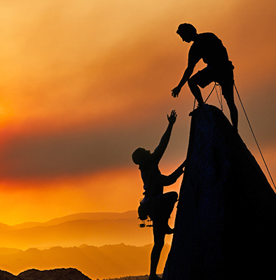 Mountain climbers, one giving the other a helping hand to get to the top.